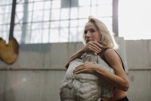 Senior woman embracing a sculpture in a sunlit studio, thoughtful and serene.