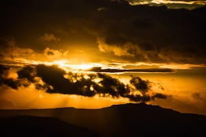 Breathtaking golden hour sunset with dramatic clouds over silhouettes of mountains.