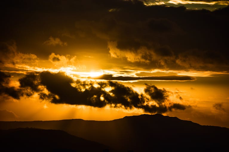 Breathtaking golden hour sunset with dramatic clouds over silhouettes of mountains.