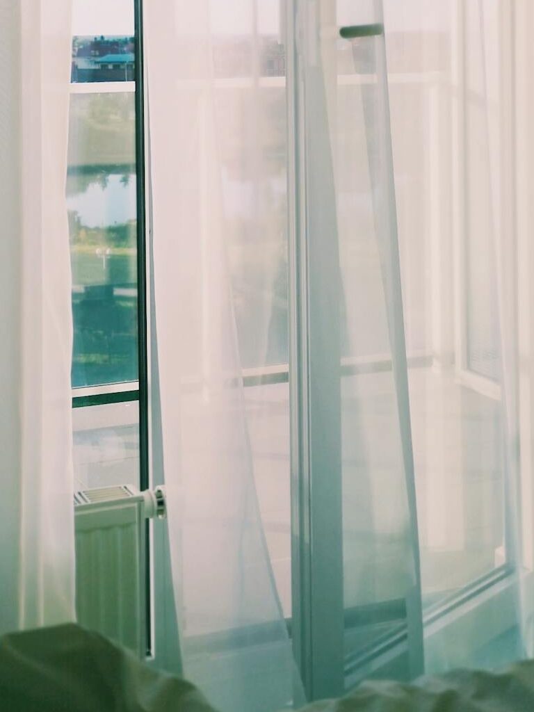 Elegant white curtains flowing with sunlight through an open balcony door, creating a tranquil indoor scene.