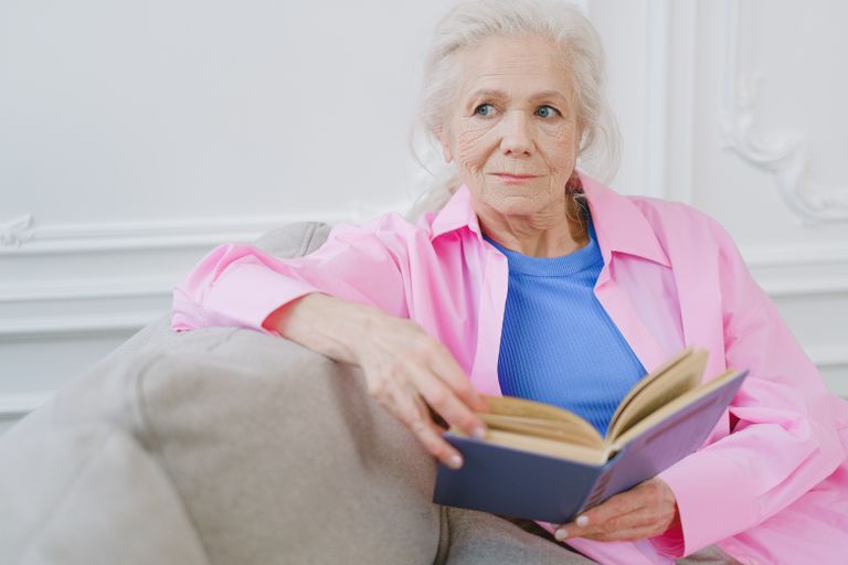 Senior woman sitting on a sofa reading a book, exuding calmness and relaxation.