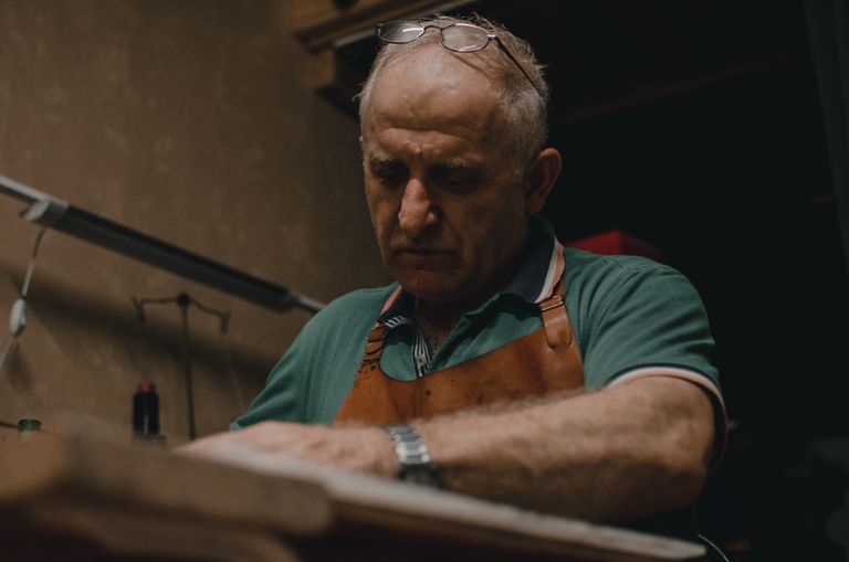 Senior artisan in eyeglasses crafting indoors with focus and skill, wearing apron.